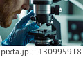 A close - up of the scientist hands - gloved hands adjust the focus of the microscope 130995918