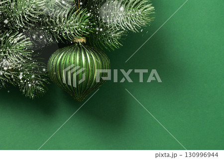 Christmas green bauble on fir snowy branch and lights garland on green background. Xmas greeting card. New Year banner. Copy space. View from above. Christmas green bauble on fir snowy branch and lights garland on green background. Xmas greeting card. New Year banner. Copy space. View from above. 130996944