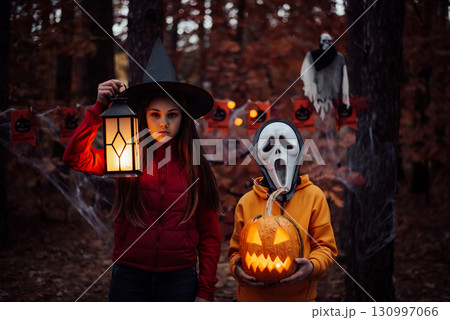 Children in halloween costumes with jack-o-lantern in dark spooky forest. Small boy in mask of a ghost, girl holding lantern 130997066