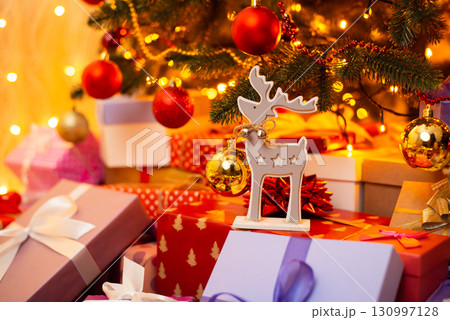 Many presents beneath christmas tree, focus on deer toy standing on boxes. Festive and cozy atmosphere of celebrating Christmas at home Many presents beneath christmas tree, focus on deer toy standing on boxes. Festive and cozy atmosphere of celebrating Christmas at home 130997128