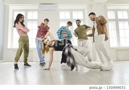 Young woman showing breakdance move on studio floor while group cheering during hip hop session. Young woman showing breakdance move on studio floor while group cheering during hip hop session. 130999031