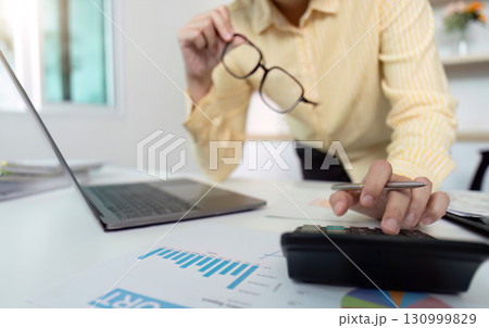 Data Review. Woman analyzing financial reports with glasses and calculator. Data Review. Woman analyzing financial reports with glasses and calculator. 130999829