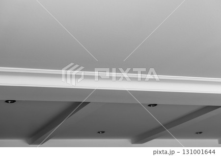 Suspended and grid ceiling with LED spots lamps and drywall construction in empty room in house interior. Stretch ceiling white and complex shape. 131001644