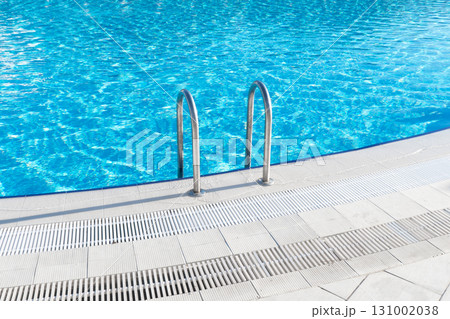 Swimming pool with stair and water. Swimming pool with handrail. Stainless steel ladder in pool. Grab bars ladder in the blue swimming pool Swimming pool with stair and water. Swimming pool with handrail. Stainless steel ladder in pool. Grab bars ladder in the blue swimming pool 131002038