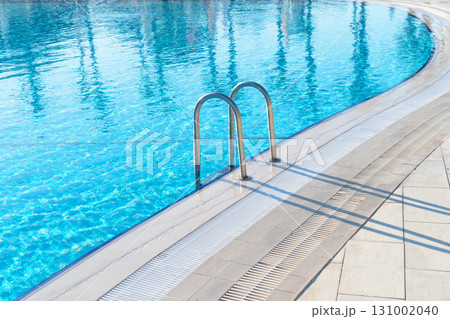 Swimming pool with stair and water. Swimming pool with handrail. Stainless steel ladder in pool. Grab bars ladder in the blue swimming pool Swimming pool with stair and water. Swimming pool with handrail. Stainless steel ladder in pool. Grab bars ladder in the blue swimming pool 131002040