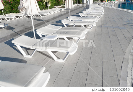Resort pool. Summer resort chair, relax lounge at luxury hotel pool. Beach lounger chaise. Vacation sunbed. Empty swimming pool with sunbed 131002049