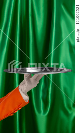 Silver serving tray held by waiter hand with glove on green curtain background 131002521
