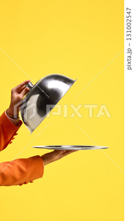 Silver cloche lifted to reveal empty tray against yellow background. Copy space for ads 131002547