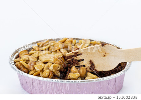 Caramel toffee cake topped with cashew nut in pink foil cup, partly eaten with wooden fork, sweet dessert, isolated on white background 131002838