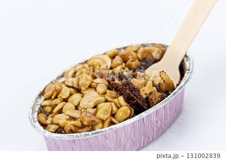 Caramel toffee cake topped with roasted peanut in pink foil container, partly eaten with wooden fork, sweet dessert, isolated on white background Caramel toffee cake topped with roasted peanut in pink foil container, partly eaten with wooden fork, sweet dessert, isolated on white background 131002839