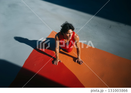 A man in a red tank top is doing a push up on a red and orange mat 131003866
