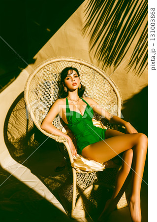 A woman is sitting in a wicker chair wearing a green bikini 131003868