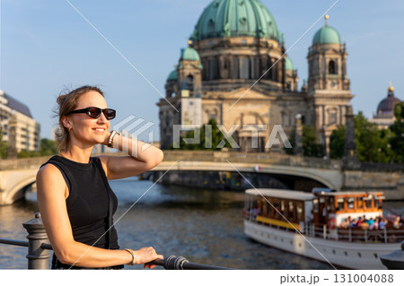 Smiling woman enjoys summer travel in Berlin standing near Spree river with cathedral and sightseeing boat in background. Scene captures spirit of tourism, culture and exploration in vibrant city Smiling woman enjoys summer travel in Berlin standing near Spree river with cathedral and sightseeing boat in background. Scene captures spirit of tourism, culture and exploration in vibrant city 131004088
