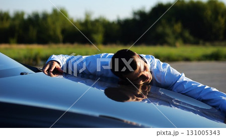 Successful smiling manager bought new electrical vehicle and hugging hood of auto. Happy young businessman in shirt enjoying modern electric automobile. Concept of buy or rent car. Slow motion 131005343