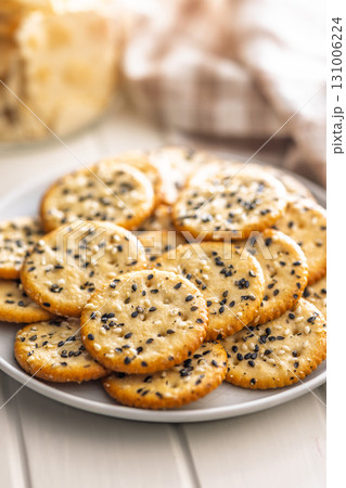 Crispy round salted crackers with sesame seeds on plate on white table. 131006224