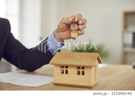 Professional real estate agent hands over keys over office table with wooden house model Professional real estate agent hands over keys over office table with wooden house model 131006549