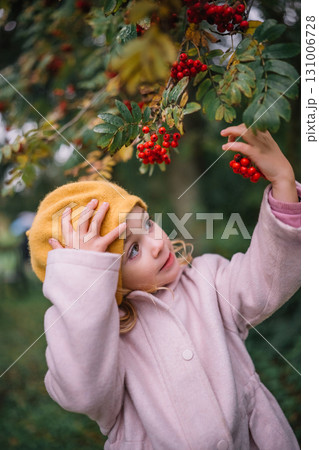 Child playing with red berries under a tree on a cool autumn day in a garden 131006728