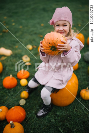 Happy child with pumpkin enjoys autumn day at a farm surrounded by harvest decorations 131006732
