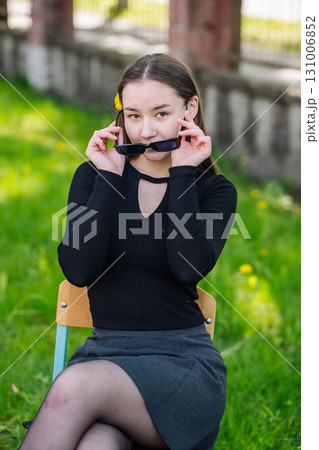 Teenage girl with dandelion in hair adjusting sunglasses while seated in schoolyard during the day Teenage girl with dandelion in hair adjusting sunglasses while seated in schoolyard during the day 131006852