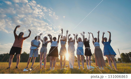 Students raising their hands at sunset in a field, celebrating their friendship and academic achievements 131006863
