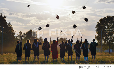 Group of graduates throwing mortarboards in the air at sunset, celebrating their academic achievement and the end of their studies 131006867