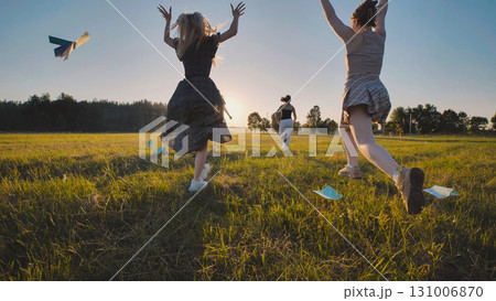 High school girls having fun running in a field at sunset, tossing paper airplanes during their summer break 131006870