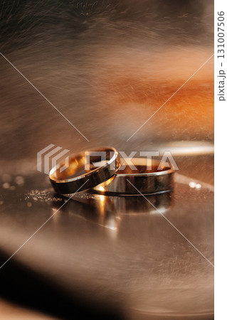Gold wedding rings on mirror surface with warm ambient light and romantic atmosphere 131007506