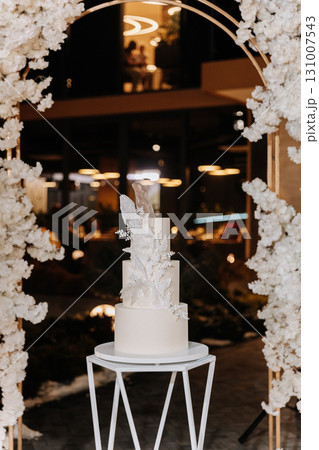 Elegant white wedding cake with sugar floral decor on modern stand at luxury reception Elegant white wedding cake with sugar floral decor on modern stand at luxury reception 131007543
