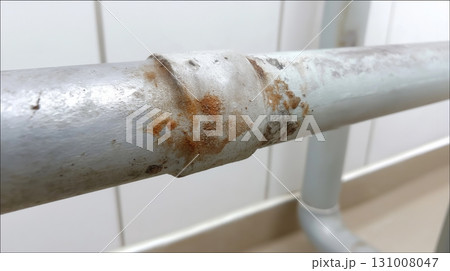 Rusty metal pipe showing wear in a modern indoor setting next to white walls 131008047