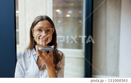 A confident woman engaging with her smartphone while in a modern office space setting A confident woman engaging with her smartphone while in a modern office space setting 131008563