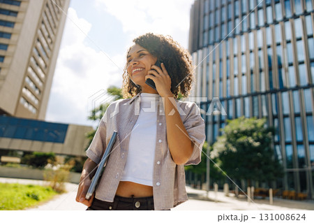 A young professional engaged in a phone conversation while surrounded by the urban landscape A young professional engaged in a phone conversation while surrounded by the urban landscape 131008624