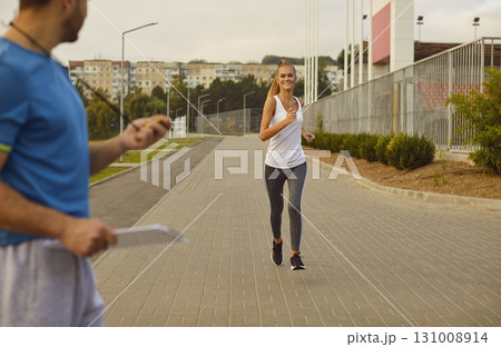 Male coach timing and checking time for performance of female happy smiling runner in a city park. Male coach timing and checking time for performance of female happy smiling runner in a city park. 131008914
