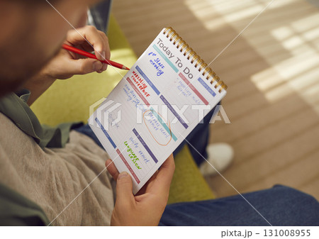 Man is writing down his daily work tasks with pencil in his paper planner notebook Man is writing down his daily work tasks with pencil in his paper planner notebook 131008955