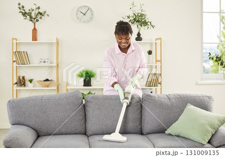 African American Woman Vacuuming Sofa At Home During Housecleaning 131009135