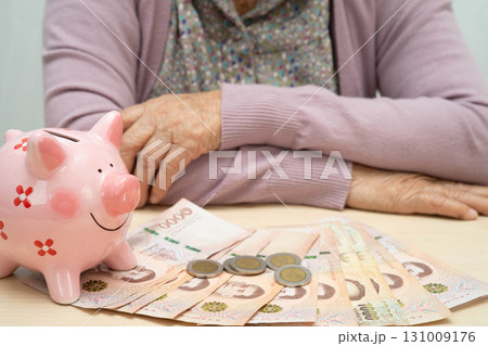 Retired elderly woman counting coins money with piggy bank and worry about monthly expenses and treatment fee payment. 131009176
