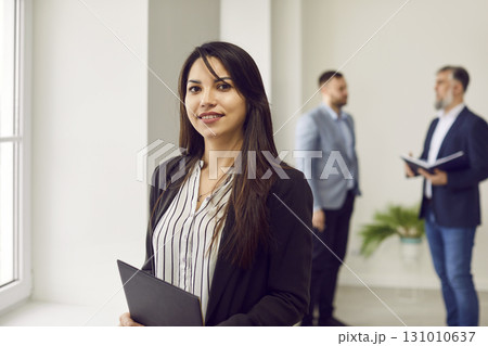 Successful businesswoman standing in office on background of colleagues Successful businesswoman standing in office on background of colleagues 131010637