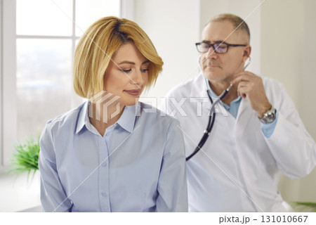 Mature patient in clinic for checkup. Doctor with stethoscope examining woman's lungs and heartbeat Mature patient in clinic for checkup. Doctor with stethoscope examining woman's lungs and heartbeat 131010667
