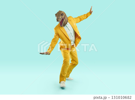 Happy man in yellow suit and funny dinosaur mask balancing on pretend skateboard 131010682