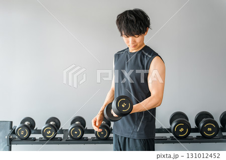 スポーツジムでダンベルを持って筋トレをする若いアジア人男性 スポーツジムでダンベルを持って筋トレをする若いアジア人男性 131012452