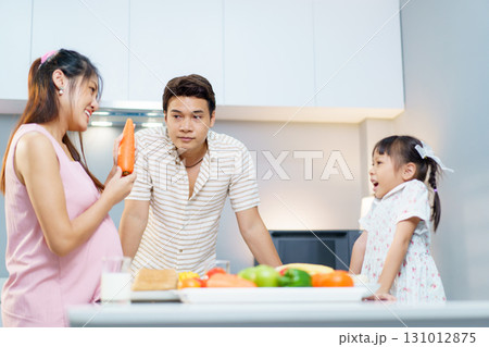 Happy Asian family including father, pregnant mother, and daughter are enjoy preparing and cooking their meal in kitchen together. Family actives in weekend concept. Happy Asian family including father, pregnant mother, and daughter are enjoy preparing and cooking their meal in kitchen together. Family actives in weekend concept. 131012875