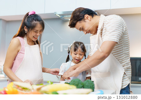 Happy Asian family including father, pregnant mother, and daughter are enjoy preparing and cooking their meal in kitchen together. Family actives in weekend concept. 131012880