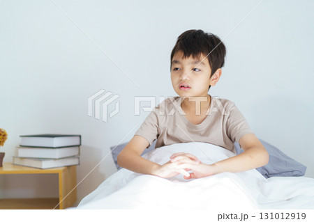 Asian boy wakes up in the early morning, feeling groggy and reluctant to leave the comfort of his bed. He yawns deeply, rubs his sleepy eyes, and stretches his arms and body lazily. Asian boy wakes up in the early morning, feeling groggy and reluctant to leave the comfort of his bed. He yawns deeply, rubs his sleepy eyes, and stretches his arms and body lazily. 131012919