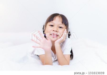 An Asian lovely little girl lying down on the bed and looking into camera with her beautiful smile on her face. A cheerful Asian cute - pretty little girl smiles to camera. An Asian lovely little girl lying down on the bed and looking into camera with her beautiful smile on her face. A cheerful Asian cute - pretty little girl smiles to camera. 131013039