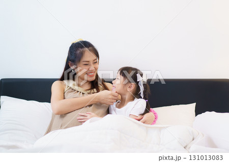 Asian pregnant woman and her lovely young daughter are relaxing and talking together while lying on the bed at night. A pregnant woman embracing her daughter on the bed in bedroom. 131013083