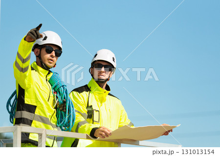 Team of professional electrical engineers in fully safety suit are working and discussing together at the windmill electric generating turbine. Electricians working at the site of windmill turbine. Team of professional electrical engineers in fully safety suit are working and discussing together at the windmill electric generating turbine. Electricians working at the site of windmill turbine. 131013154