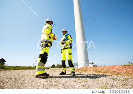Team of professional electrical engineers in fully safety suit are working and discussing together at the windmill electric generating turbine. Electricians working at the site of windmill turbine. 131013158