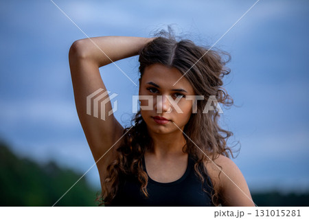 A Young Woman with Beautiful Curly Hair Posing Outdoors in the Soft Light of the Golden Hour A Young Woman with Beautiful Curly Hair Posing Outdoors in the Soft Light of the Golden Hour 131015281