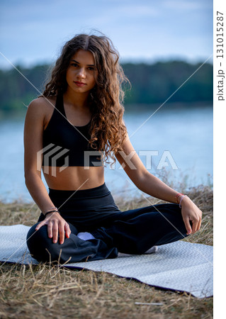 A young woman practicing yoga by the water, embodying serenity and balance in nature 131015287
