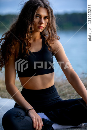 A young woman practices yoga by the serene waters edge, embodying balance and calm 131015288