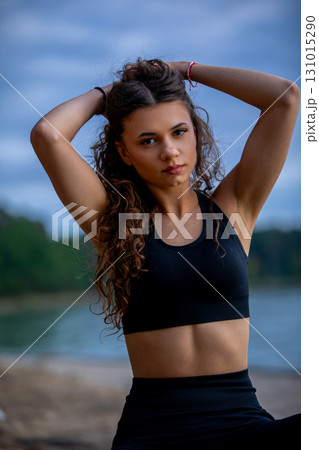 A young woman poses confidently by the water in stylish fitness attire, showcasing beauty 131015290